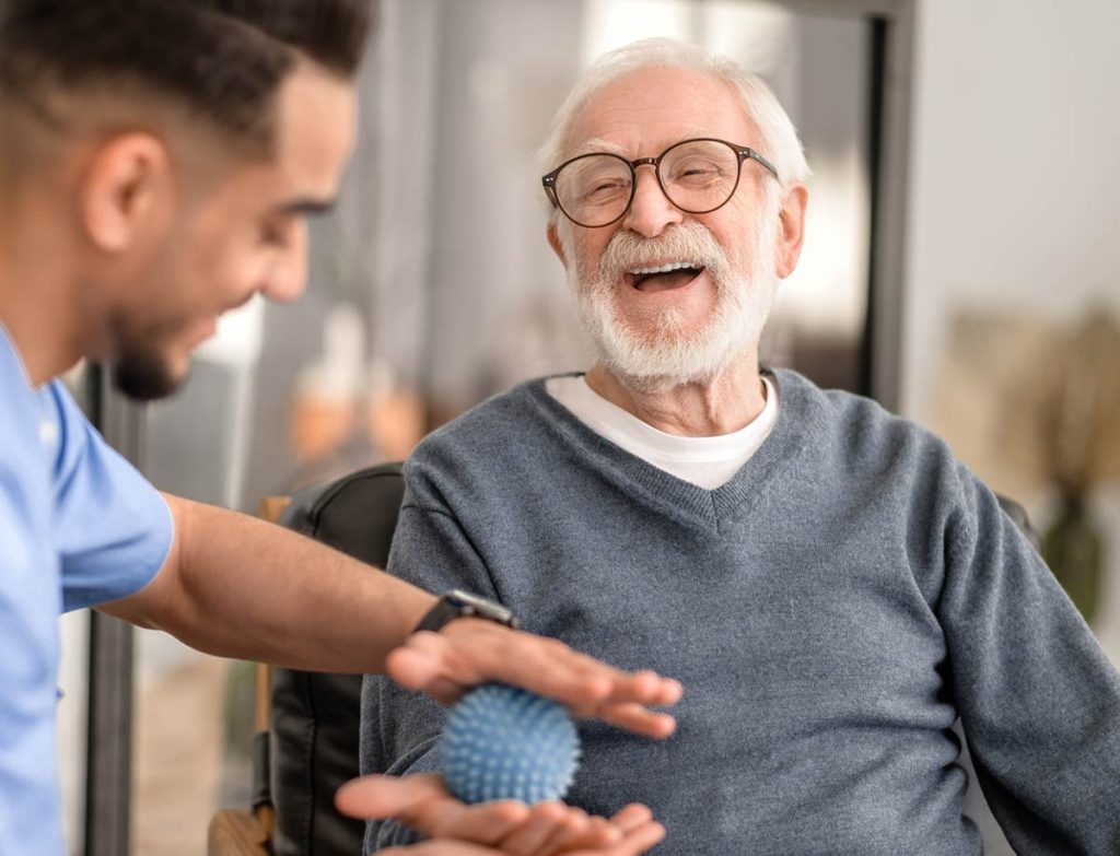 Senior gentleman laughing while doing physical therapy with physio.